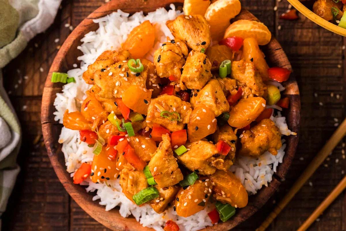 Tangerine chicken on top of white rice in a bowl.