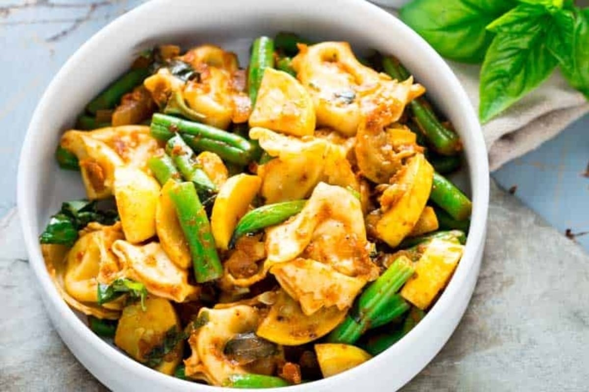 A delicious recipe featuring tortellini and fresh green beans, elegantly served in a white bowl.