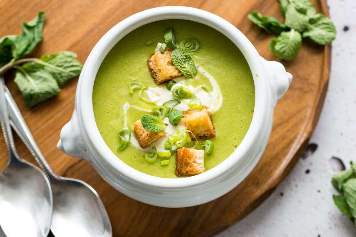 A bowl of green soup with croutons and mint.