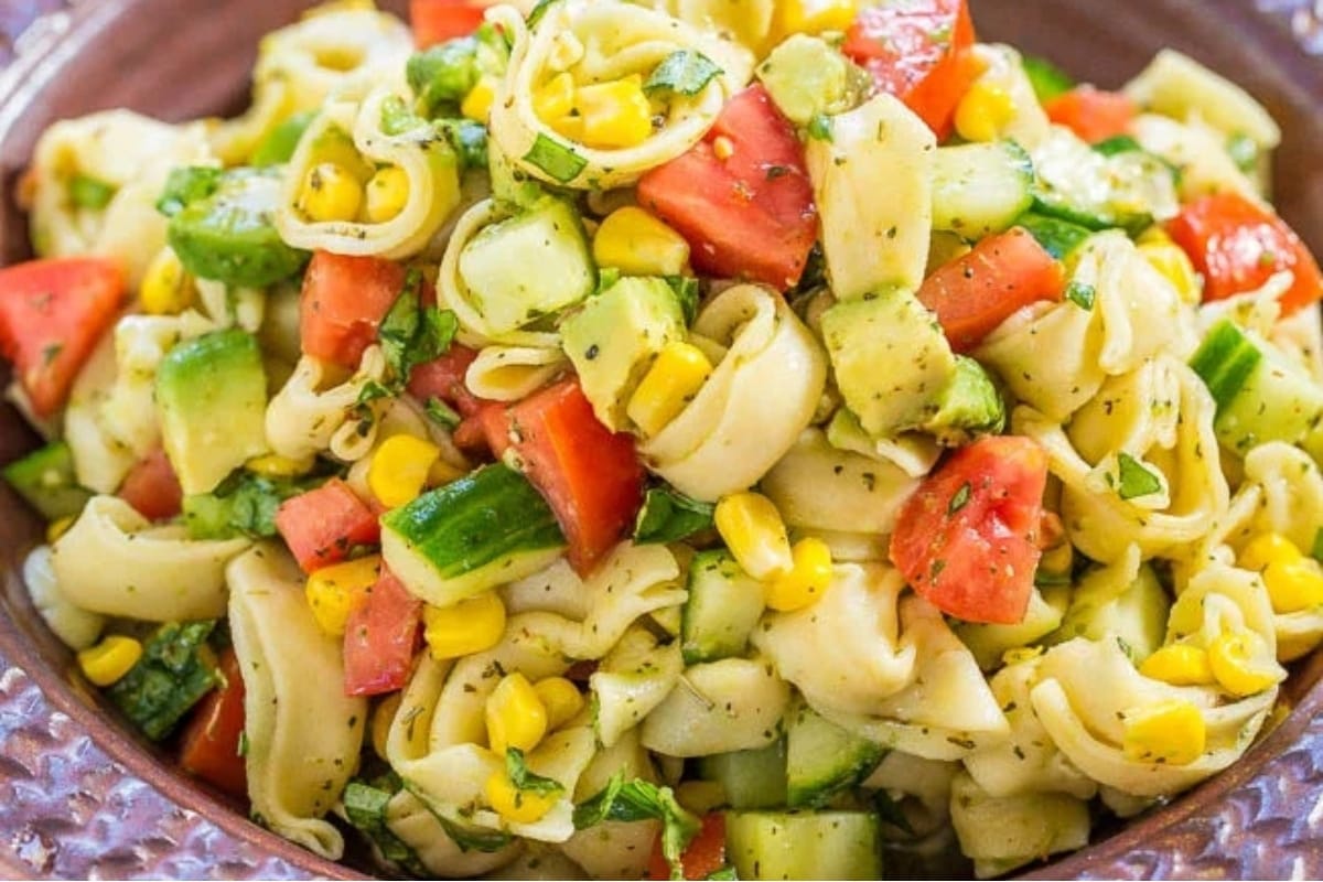 A refreshing bowl of pasta salad with tomatoes and cucumbers, perfect for summer gatherings.