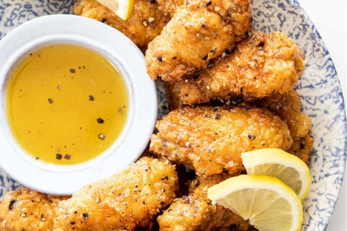 Bite-sized chicken wings on a blue plate with lemon wedges.