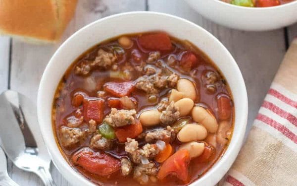 Sausage and bean soup in a white bowl with a striped cloth.
