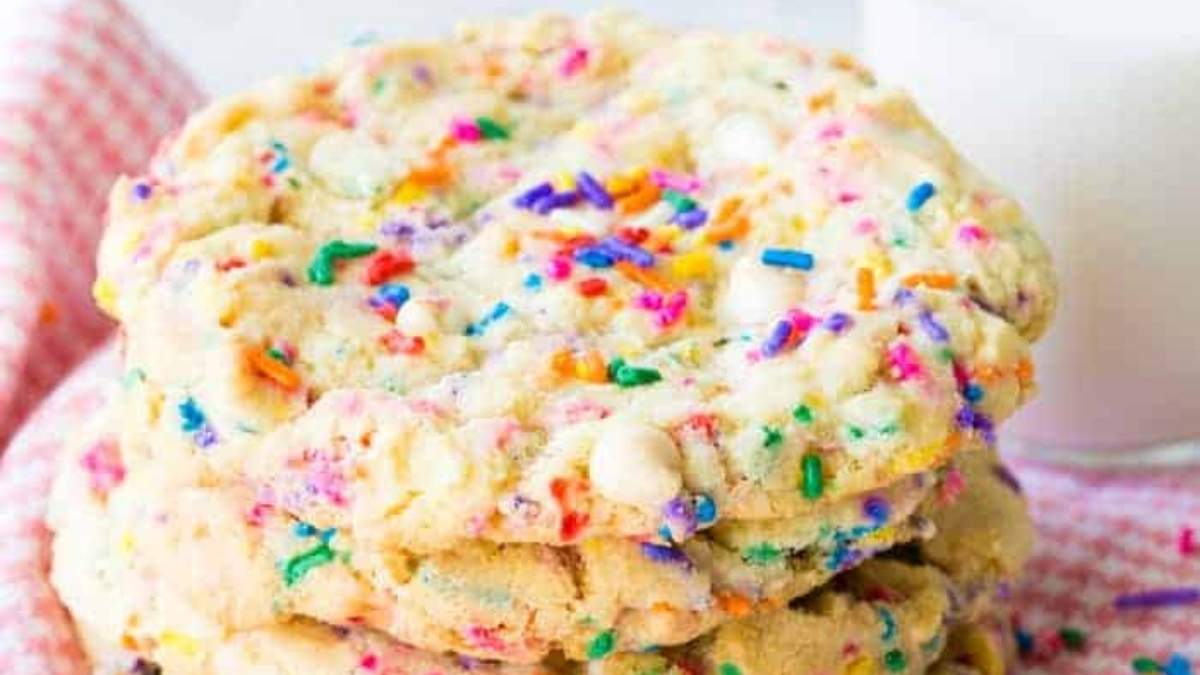 A stack of rainbow sprinkle cookies next to a glass of milk. These delicious treats are sure to satisfy your sweet tooth and are the perfect accompaniment to a cold glass of milk.