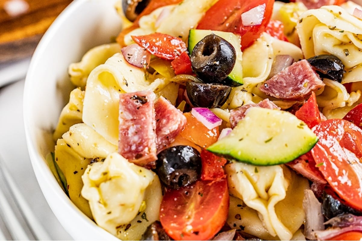 Tortellini salad with ham and vegetables in a white bowl. Have you ever tried tortellini salad before? This delicious dish combines tender tortellini with savory ham and fresh vegetables, all