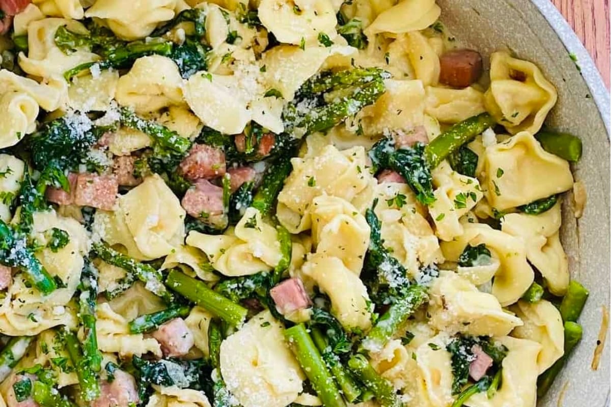 Tortellini and asparagus pasta in a skillet on a wooden table.