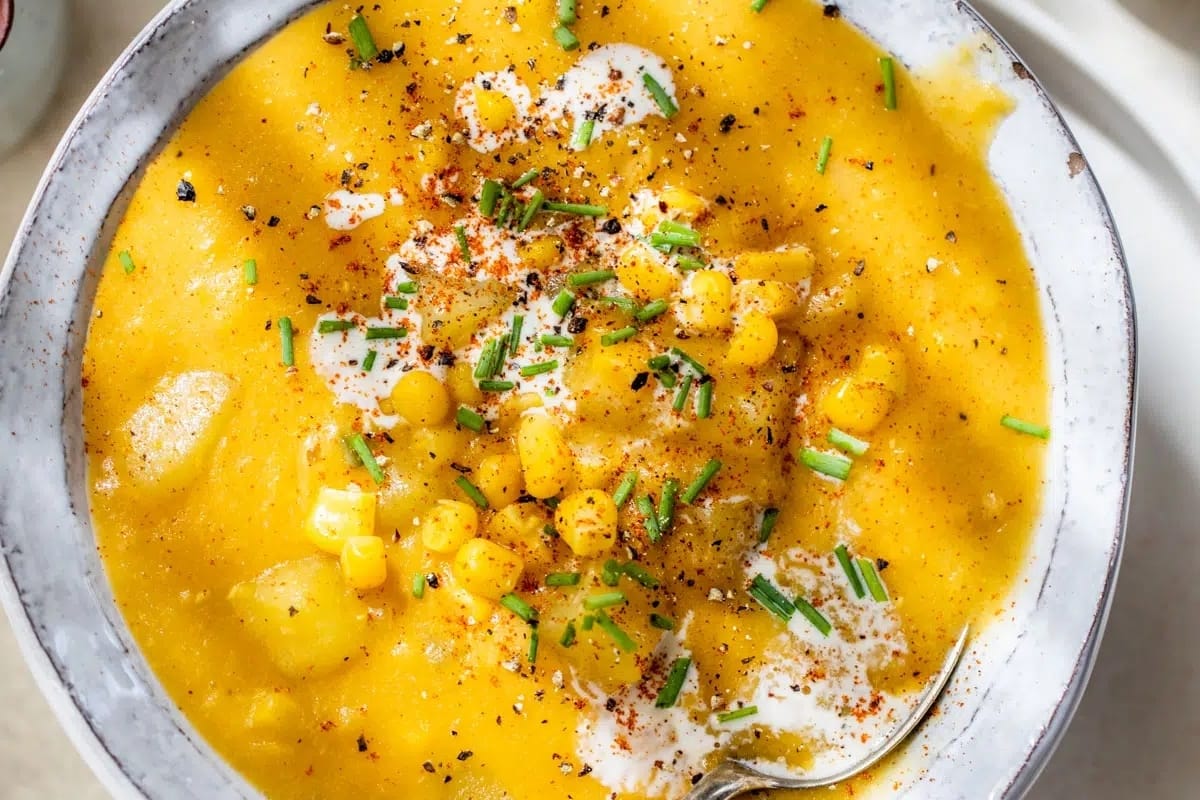 A hearty bowl of yellow corn chowder soup, served with a spoon.