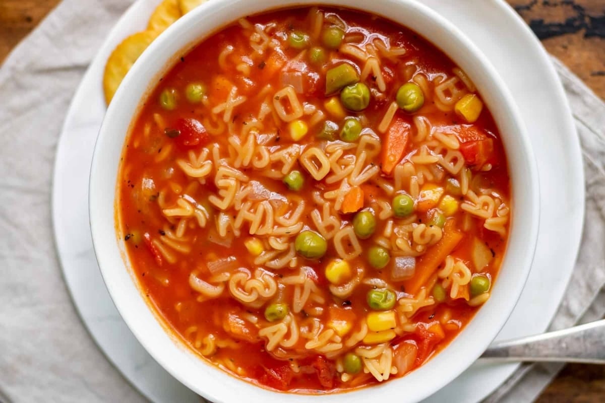 A bowl of noodle soup with mixed vegetables and peas.