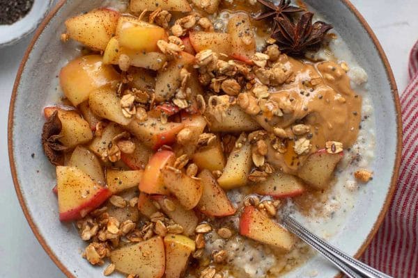A bowl of oatmeal with apples and peanut butter.
