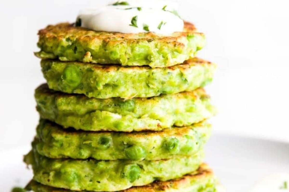 A stack of green pea pancakes with sour cream.