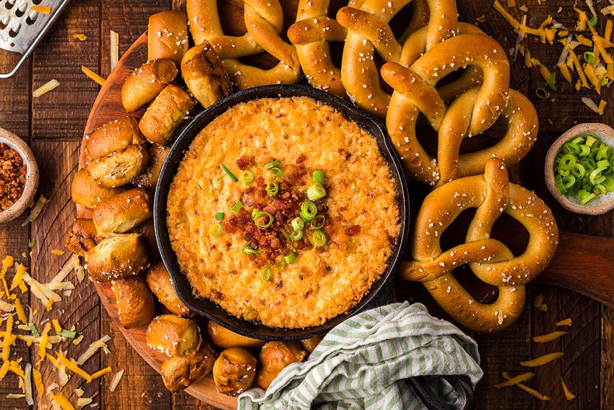 Smoked Gouda cheddar bacon dip in a bowl with pretzel options around it.