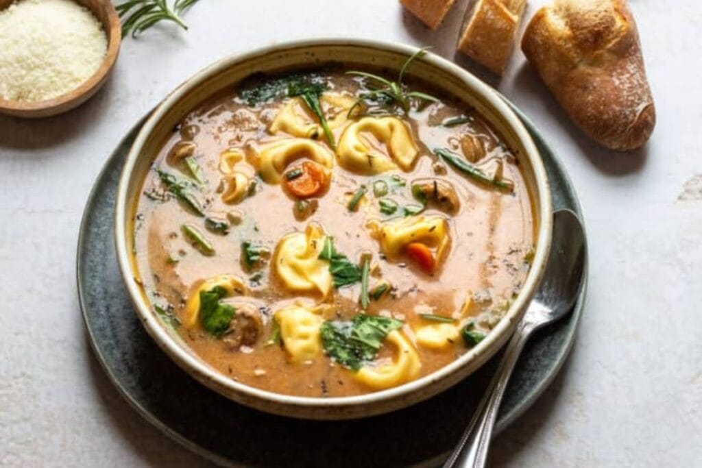 Tortellini soup with sausage in a bowl with bread.