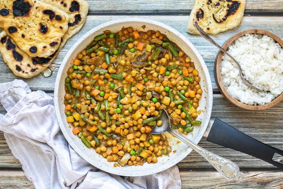 Chickpeas, rice, and frozen mixed vegetables in a pan on a wooden table.