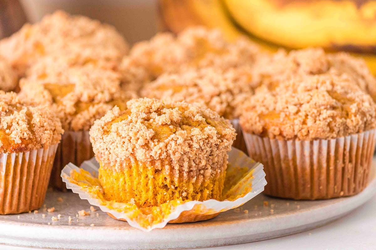 Banana pumpkin muffins with one on top that is sliced in half, revealing the texture of the muffin.