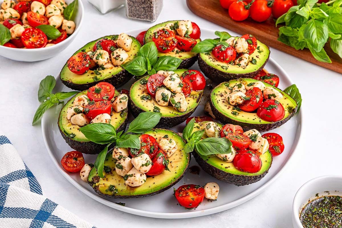 Caprese stuffed avocado on a plate with fresh basil leaves.