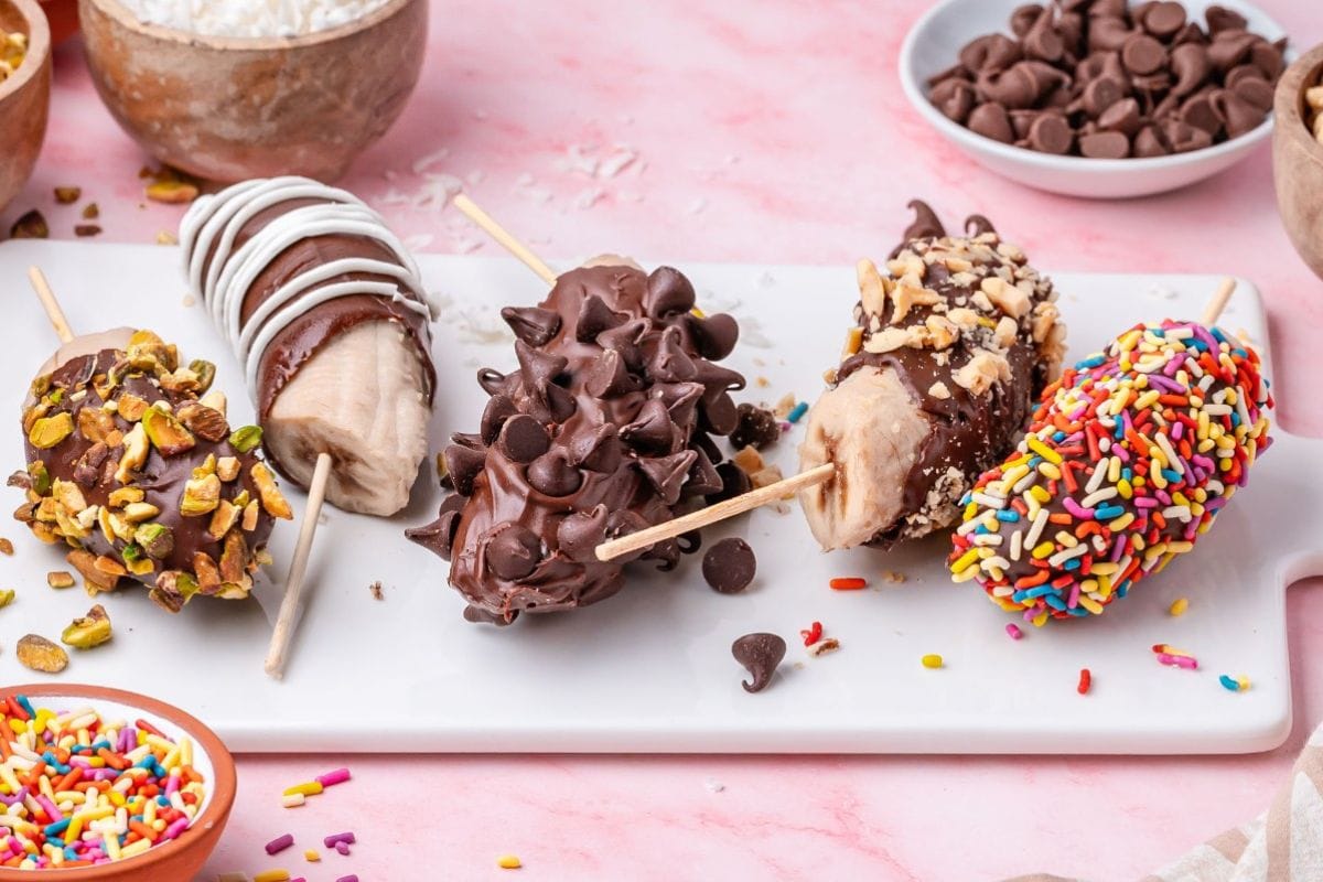 Two frozen chocolate-covered bananas on sticks - one is covered with nuts and the other with sprinkles. 