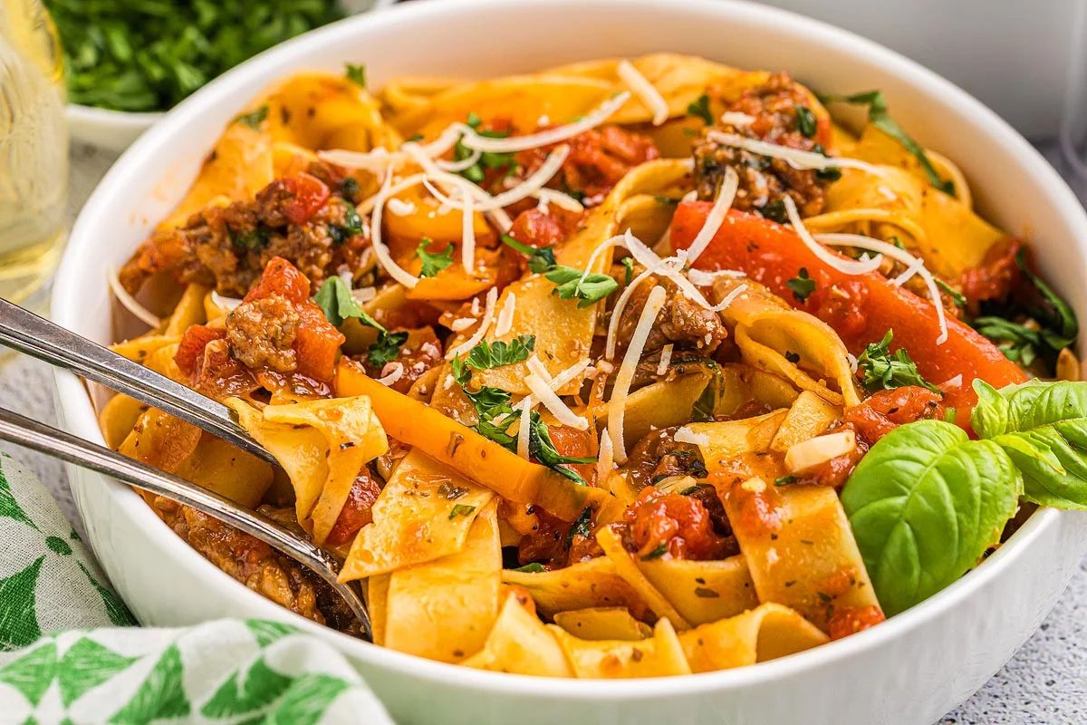Italian drunken noodles with wooden serving spoons in a large white bowl.