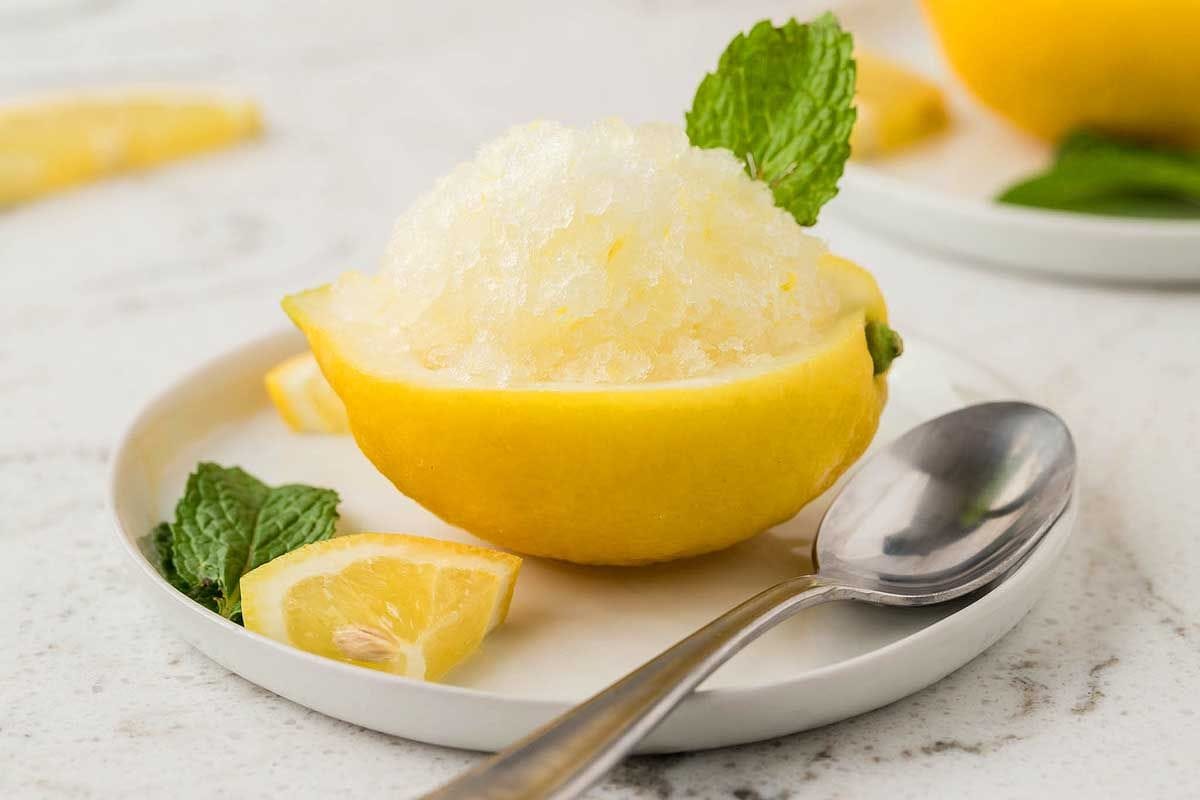 Lemon granita (granita al limone) served in a halved lemon in a white plate.