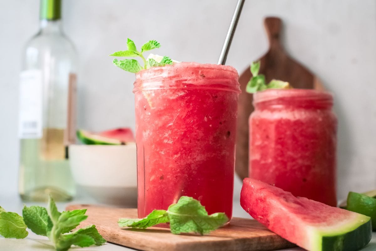 Summertime watermelon white wine slushie in a mason jar on a cutting board with mint and watermelon slices.
